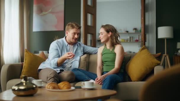 快乐的一对在周末公寓聊天 情绪化的男人向妻子讲有趣的故事 微笑的女人听着丈夫在笑 喜欢在家里吃早餐的人舒服的沙发 家庭概念 — 图库视频影像