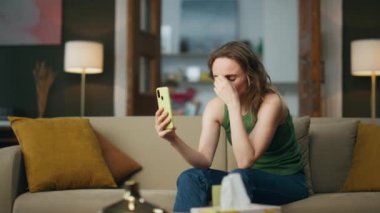 Kanepede akıllı telefondan konuşan ağlayan kadın. Oturma odasında cep telefonuyla konuşan depresif bir kadın. Mutsuz kız koltukta otururken cep telefonuyla video görüşmesi yapıyor. Sinirli insan evde sorunlardan şikayetçi.