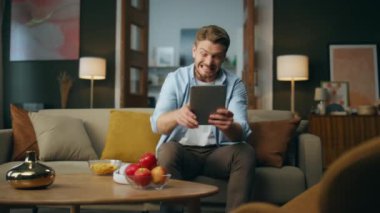 İç mekanda el kol hareketini kazanan heyecanlı adam. Başarıyı kutlayan aşırı neşeli hipster. Duygusal adam modern odada tablet ekranı seyrediyor. İş adamı kavram kazanıyor 