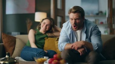 Akşam evde futbol taraftarları kök saldı. Genç çift kanepede oturup televizyon maçı izliyor. Duygusal adam gol zaferini coşkuyla kutluyor. Kocasının kanepeye gülüşü. 