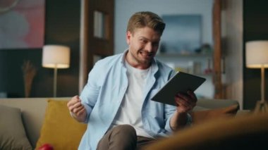 Memnuniyetle kazanan iç mekanda evet işareti yapıyor. Heyecanlı adam neşeli duygular gösteren tablet kutluyor. Başarılı kazanma projesini kutlayan mutlu adam. Serbest yazar başarıların ve iyi sonuçların tadını çıkarıyor