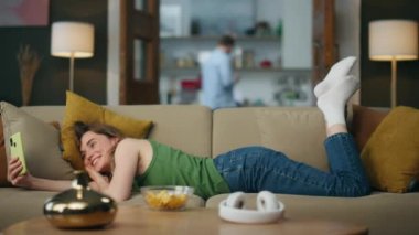 Kanepenin içini arayan tembel kız videosu. Gülümseyen kadın yastığını dinlendirirken telefon konferansında yalnız konuşuyor. Dost canlısı bayan en iyi arkadaşıyla konuşuyor rahat koltukta cep telefonuyla sohbet ediyor.