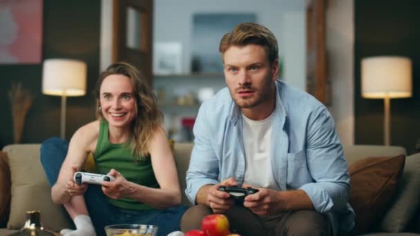兴奋的夫妻在家里玩电子游戏 两个朋友在舒适的公寓里玩控制台 恶心的男人从女人手里接过游戏垫 老婆老公在沙发上玩得开心 — 图库视频影像