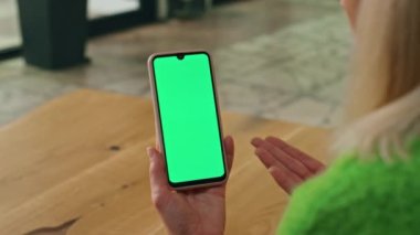 Kapalı alanda elinde yeşil ekran telefon tutan bir kadın. Ofisteki Chromakey akıllı telefonu arayan bilinmeyen bir çalışan videosu. Kadın yönetmen el hareketleriyle ekrandaki cep telefonu görüntüsünü yakınlaştırıyor.