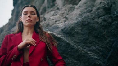 Kayalık doğa bulutlu bir günde kameraya poz veren göz kamaştırıcı kadın. Dağlarda seksi kırmızı takım elbiseli, kendine güvenen zarif bir kız. Güzel, sakin bir kadının portresi. Kasvetli gökyüzünün önünde..