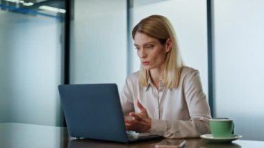 Ciddi bir iş kadını konferans odasından laptop 'ı arıyor. Odaklanmış girişimci, web kamerasıyla uzaktaki web sitesinde tek başına konuşuyor. Akıllı kadın internette video konferansında açıklıyor. 
