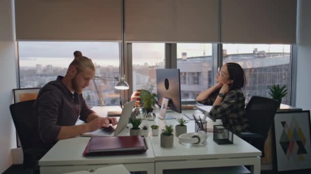 精疲力尽的女人在日落办公室里伸懒腰 专心致志的男人在桌旁打字 同事们准备在全景窗口工作场所截止日期 人们晚上工作到很晚 — 图库视频影像