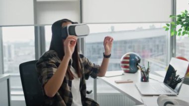 Ofis kapanışında VR nesnelerini değiştiren odaklı programcı. Gelişmiş gerçeklikte el kol hareketi yapan modern kulaklıklı kadın. Panoramik pencerelerdeki görünmez arayüze dokunan tasarımcı