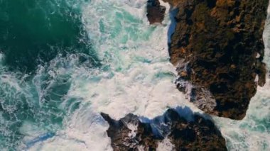 Kıyı kayalıklarını kıran dalgalı okyanus dalgaları beyaz köpüğü yavaş çekime sokuyor. Köpüklü deniz suyu volkanik taşların üzerine sıçrıyor. Nefes kesen hava manzaralı fırtınalı akıntı kıyı kayalarını çarpıyor..