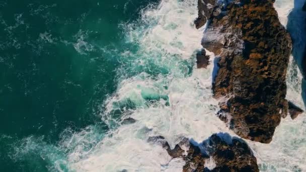 泡沫般的海水在沿海的峭壁上飞溅 汹涌的蓝色海浪以缓慢的海岸运动冲撞火山岩 电影中的空中风景粗野地冲破了多石的海岸线 海洋风景秀丽 — 图库视频影像
