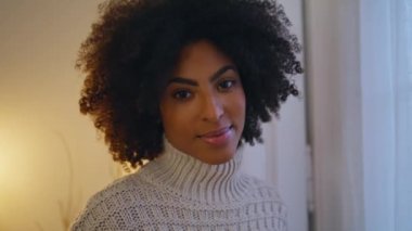 Otel odasında poz veren sakin bir portre modeli. Kıvırcık saçlı romantik kız perdelere yakından bakıyor. Afro-amerikan bayan akşam ışığında ayakta duruyor. Sakin koyu tenli kadın yalnız dinleniyor.