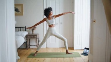 Esnek bir kadın rahat bir yerde uzanıyor. Kıvırcık saçlı sporcu yoga halısında Asana antrenmanı yapıyor. Yogi modeli tablet kullanarak video eğitimi izliyor. Afrikalı kız tek başına çalışıyor. Uyumlu yaşam tarzı kavramı 