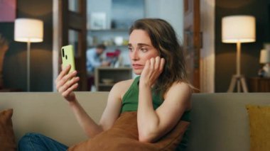 Üzgün bayan, akıllı telefondan ev kanepesinde konuşuyor. Depresyondaki kadın oturma odasında cep telefonuyla görüntülü konuşma yapmaktan şikayetçi. Mutsuz bir kız cep telefonunu arıyor, koltukta oturuyor. Sorun kavramı