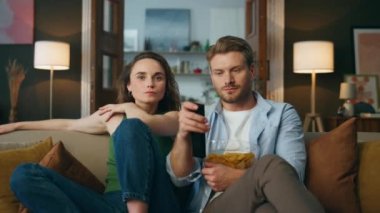 Mutlu çift kanepede oturuyor ve evde televizyon seyrediyor. Sakallı adam uzaktan kumandalı kanal değiştiriyor. Genç ve rahat eşler televizyon izleyerek kanepede zum yapıyorlar. Eğlence konsepti 