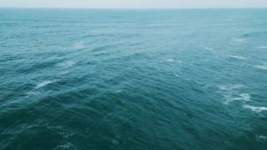 Panoramik hava manzaralı akşam deniz manzaralı sakin mavi okyanus suyu çok yavaş dalgalanır. Bulutlu gökyüzü altında deniz dalgaları. Yaz günü. Köpüren dalgalarla sakin, kasvetli deniz manzarası. Doğa yolculuğu.
