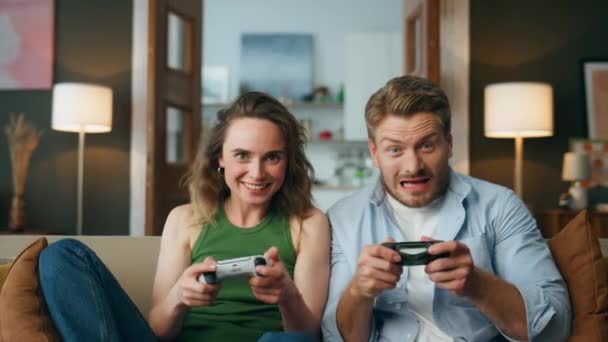 喜形于色的朋友们喜欢在家里玩电子游戏 兴奋的游戏玩家拿着游戏面板竞争视频 一对无忧无虑的夫妻坐在沙发上消磨时光 玩的开心 业余时间的概念 — 图库视频影像
