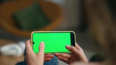 Oyuncu evde kromakey oynayan cep telefonu kullanıyor. Kimliği belirsiz bir kadın salonda tek başına akıllı telefon ekranına dokunuyor. Modern kız elleri video oyunu oynarken yeşil ekran cep telefonunu tıklatıyor
