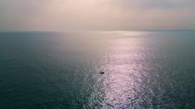 Sonsuz okyanus manzarasında yüzen yalnız bir tekne. Motorlu yat harika bir derin deniz körfezi geziyor. Sakin su yüzeyine yansıyan parlak güneş ışığı. Denizcilik yaz ufkunda gemi gezisi. Huzur kavramı