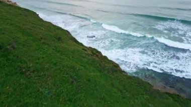 Fırtınalı deniz kıyısı yeşil tepeler insansız hava aracı manzaralı. Güzel okyanus dalgaları bulutlu yaz havasında kumlu kıyıları yıkıyor. Karanlık derin deniz yüzeyi ufku. İnanılmaz dramatik deniz doğası konsepti