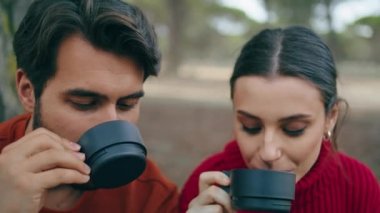 Sonbahar doğasında piknikte sıcak içecek içen sevimli bir çift. Yakın plan. Parkta kahve içen rahat gülümseyen bir kadının portresi. Romantik turistler dışarıda birlikte dinleniyorlar.