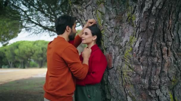 秋の公園でキスをする素敵な若いカップルが広い木の近くにもたれています 自然の中で週末を過ごす一緒に巨大な立って美しい柔らかい家族のペア 幸せな人々はロマンチックなデートで感情を楽しむ — ストック動画