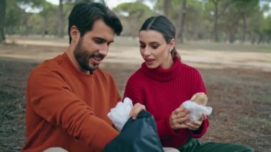 Güzel parkta piknik battaniyesi hazırlayan gülümseyen, rahat bir çift. Sırt çantasından yemek içen mutlu sakallı adam. Tasasız aile romantik hafta sonunun tadını çıkarır. Boş zaman konsepti