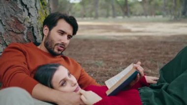 Güzel, kaygısız bir çift kitap kapanışı ile parka uzandı. Çekici sakallı adam güzel bir kadın için yüksek sesle okuyor. Sakin bir kadın erkek arkadaşının göğsünde dinleniyor. Mutlu genç çift ormanda birlikte vakit geçiriyor.