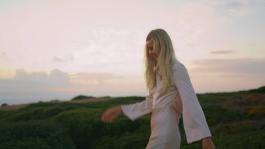 Durgun model gülen tepeler, sakin doğa yaklaşımında. Elbise giymiş, günbatımı sahili pozu veren çekici bir kız portresi. Genç bayan yeşil vadiyi rahatlatan kameraya bakıyor. Sarışın kadın geceyi yalnız geçiriyor.