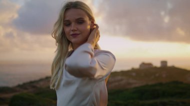 Romantik model akşam zum yaparken doğayı rahatlatıyor. Sonbahar ortamında el kamerasını esneten olumlu bir kadın. Sarışın kız saçlarına dokunuyor rüzgarlı havalarda okyanus arka planında dinleniyor.