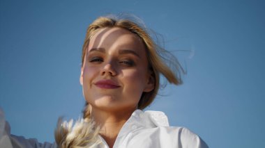 Sunny model mavi gökyüzü arkaplanı. Gülümseyen kız kameraya bakıp yüzünü kapatıyor. Şefkatli bayan rüzgârlı yaz doğasında yalnız vakit geçiriyor. Sarışın kadın baştan çıkarıcı bir şekilde merceğe bakıyor.