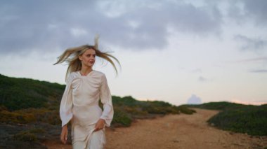 Yeşil bitkilerle tepede koşan neşeli kız. Mutlu kadın gün batımında hiç dokunulmadan hızla ilerliyor. Sarışın manken akşam manzarasının tadını çıkartıyor. İnsanlar ve çevre kavramı