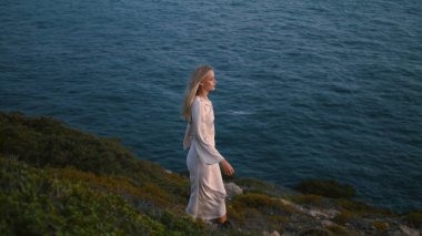 Okyanus uçurumunda tek başına yürüyen düşünceli bir kadın. Hayalperest kız yaz akşamı Marine View Hill 'e ayak basıyor. Rahatlamış bayan dinleniyor ve güzel günbatımının tadını çıkarıyor. Sarışın model deniz suyu manzarasında seyahat ediyor.