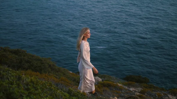 一个有思想的女人独自走在悬崖上 梦寐以求的女孩在夏夜踏上海景山 放松的女士休息 享受美丽的日落自然 Blonde模型航行的海水景观 — 图库照片