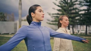 Yogi kadınları parkta silah eğitimi alıyorlar. Yeşil doğa mekanında sabah yoga egzersizleri yapan iki odaklanmış kadın. Formda kız arkadaşlar derin sıcak kol kasları soluyor.