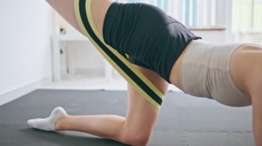 Kapalı kadın vücut egzersizi evde. Direnç bandı egzersizi yapan sporcu kadın arka bacak kaslarını esnetiyor. Atletik güçlendirilmiş kız tek başına kalori yakıyor. Sabah sporu
