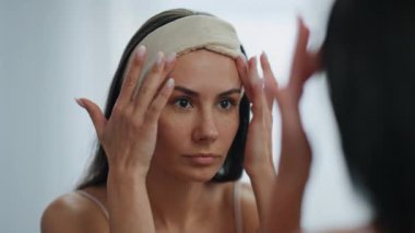 Aynalı mekanda endişeli kadın yüz kırışıklıkları sorunu. Kapanış stresi çeken kadın, yaşlanma karşıtı yüz yogası egzersizlerinin kötü sonuçlarından rahatsız oluyor. Üzgün model kas durumunu kontrol ediyor. Doğal güzellik.