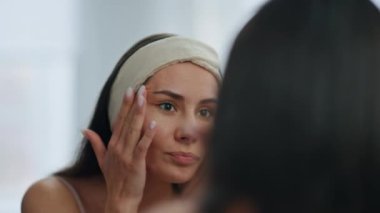 Hayal kırıklığına uğramış kız banyoda aynaya bakıyor. Yakın çekim. Evde sivilcelerden rahatsız olan kuru ve kırılgan bir cilde üzülüyor. Mutsuz stresli kadın, kırışıklıkları kontrol ediyor. Yüze dokunuyor. Yüz problemi kavramı