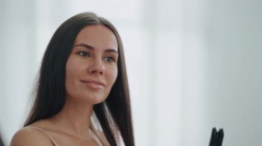 Güzel model saçına dokunuyor ve evde keyif çatıyor. Banyodaki aynaya bakan tatmin olmuş bir kadın. Gülümseyen kadın tek başına profesyonel düzleştirici kullanarak şövalye stili yapıyor. Doğal güzellik konsepti