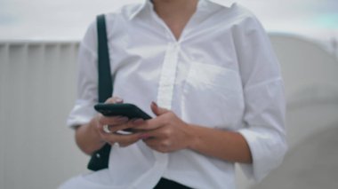 Unknown stylish business woman messaging on modern smartphone walking city street close up. Female hands holding black telephone typing on screen. Unrecognizable elegant lady texting sms on go outdoor