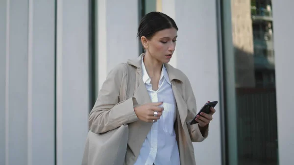 stock image Busy elegant girl received phone message going on work near modern building closeup. Attractive young business woman walking street looking telephone screen. Confident lady hurrying office with mobile