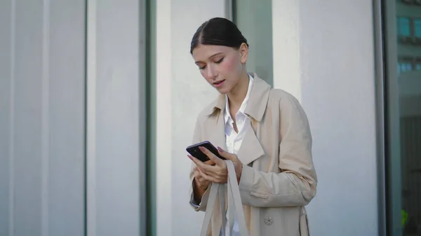 stock image Preoccupied young woman answering phone standing on city street alone. Busy business lady starting telephone conversation outdoors near office building. Attractive elegant girl talking on smartphone.