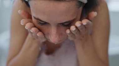 Yakın çekim modeli evde deriyi suyla yıkıyor. Portre gülümseyen kız pencerenin önündeki kameraya bakıyor. Rahat kadın sabah rutini. Cilt bakımı ve yüz temizliği konsepti