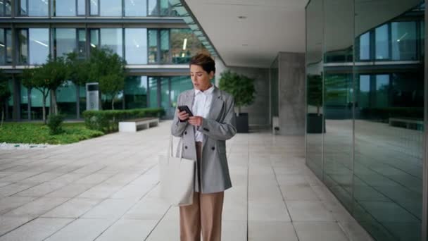 ダウンタウンのビジネスセンターで女性エグゼクティブタイプの携帯電話 焦点を当てた女性は屋外のパートナーとスマートフォンチャットを保持します 中年の実業家のウェブチェックメールを閲覧 金融銀行アプリ — ストック動画