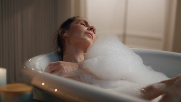 落ち着いた女性が泡風呂をリラックス リラックスした女性は 夕方のバスルームで一人でバスタブを取る肌を洗う 居心地の良い家で安静に裸の体感覚に触れるブルネットモデル 国内温泉と健康 — ストック動画