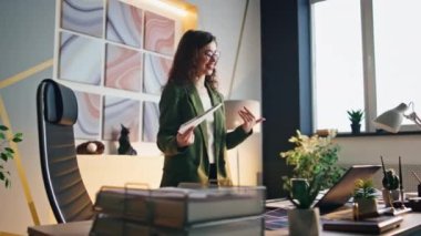Gülümseyen kadın çalışanlar modern ofiste online iletişimin keyfini çıkarıyorlar. Çekici, mutlu iş kadını iş arkadaşlarıyla video konferansında gülüyor. Dizüstü bilgisayar kamerasına bakan genç bir yönetici.