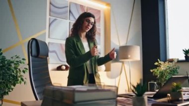 Başarılı kadın yönetici modern işyerinde çevrimiçi konferans düzenliyor. Partnerlerle konuşan mutlu iş kadını işten memnun. Kumral CEO ofisinde baş parmağını gösteriyor..