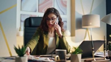 Gergin kadın yönetici modern ofis masasında otururken telefonu arıyor. Tasarım örnekleriyle ilgilenen yaratıcı direktör iş sonucu için endişeleniyor. Stresli kız akıllı telefondan konuşuyor.