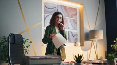 Genç ciddi iş kadını ofisinde telefonla konuşuyor. Kendine güvenen çekici kız menajer iş belgelerine bakıyor telefonda konuşuyor. Kadın patron akıllı telefondan iş meselelerini tartışıyor..