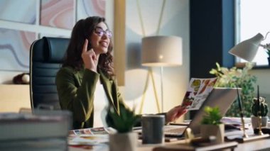 Gülümseyen neşeli iş kadını internette sohbet ediyor modern ofiste dizüstü bilgisayarla oturuyor. Mutlu kreatif direktör videodaki ekibiyle konuşuyor memnun şirket işleri. İş başarısı konsepti.