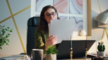 Çekici kız şirket çalışanı cep telefonuyla konuşuyor ofis masasında oturuyor, yakın plan. Akıllı telefondan şirket sorunlarını tartışan memnun bir çalışan. İş kadını iş yerinde iş belgelerini tutuyor